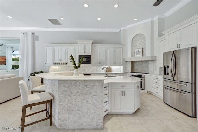 kitchen with white cabinets, a center island with sink, appliances with stainless steel finishes, and decorative backsplash