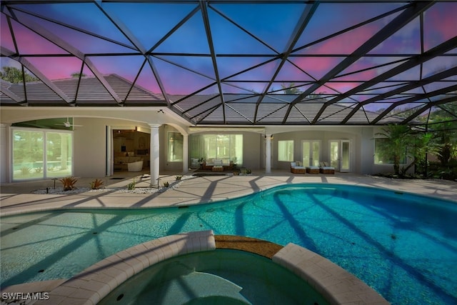 pool at dusk featuring ceiling fan, a lanai, a patio, and an in ground hot tub