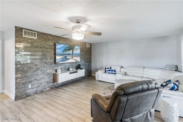 living room with a textured ceiling, light wood-type flooring, and ceiling fan