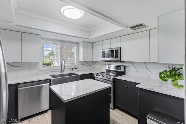 kitchen featuring white cabinetry, light wood-type flooring, stainless steel appliances, sink, and a center island