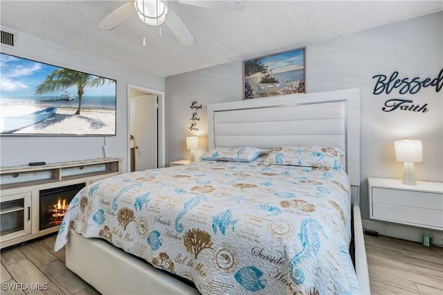 bedroom featuring ceiling fan, a fireplace, a textured ceiling, and light hardwood / wood-style floors