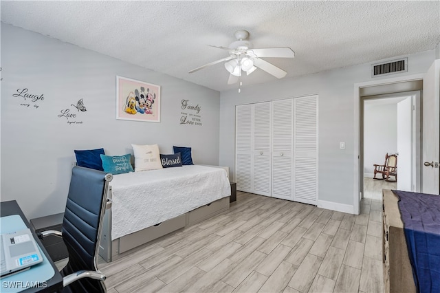 bedroom with light hardwood / wood-style flooring, a textured ceiling, a closet, and ceiling fan