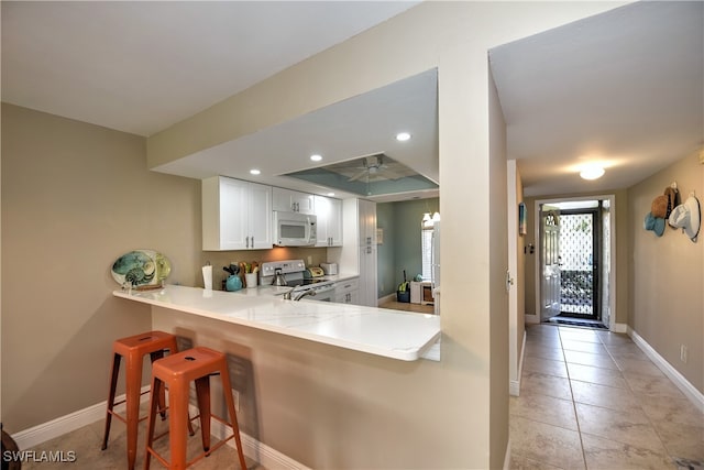 kitchen with kitchen peninsula, white cabinetry, stainless steel electric range oven, ceiling fan, and a breakfast bar area