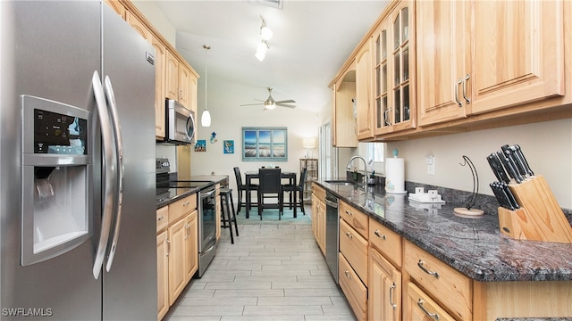 kitchen with lofted ceiling, dark stone counters, sink, light brown cabinets, and appliances with stainless steel finishes