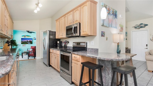 kitchen featuring hanging light fixtures, light brown cabinetry, a breakfast bar, and appliances with stainless steel finishes