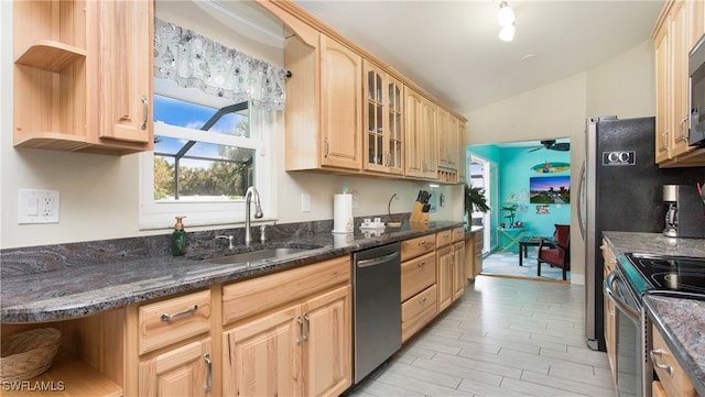 kitchen featuring stainless steel appliances, sink, light brown cabinetry, dark stone countertops, and lofted ceiling