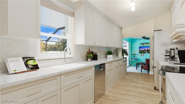 kitchen with tasteful backsplash, stainless steel appliances, light wood-type flooring, light stone countertops, and sink