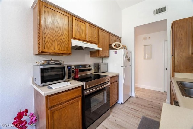 7925 Preserve Cir Unit 333, Naples, FL 34119 - kitchen with under cabinet range hood, stainless steel appliances, light countertops, light wood-type flooring, and brown cabinetry