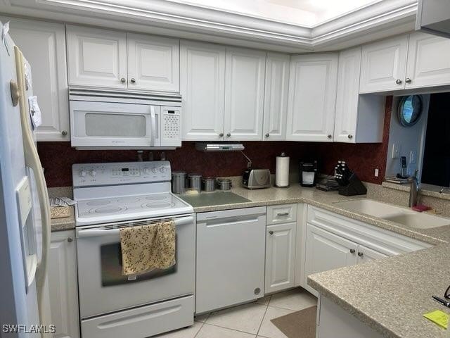 kitchen with light tile patterned flooring, white cabinetry, decorative backsplash, sink, and white appliances