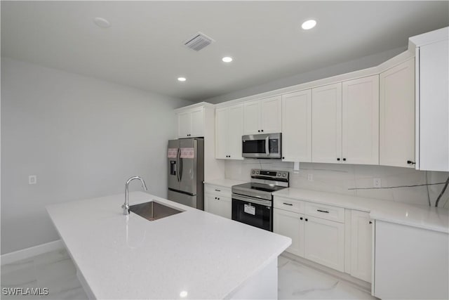 kitchen featuring decorative backsplash, a kitchen island with sink, white cabinets, appliances with stainless steel finishes, and sink