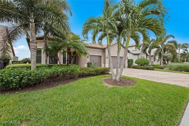 mediterranean / spanish-style home with an attached garage, a tile roof, decorative driveway, stucco siding, and a front yard