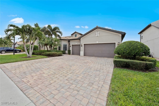 view of front of house with an attached garage, a tile roof, decorative driveway, stucco siding, and a front yard