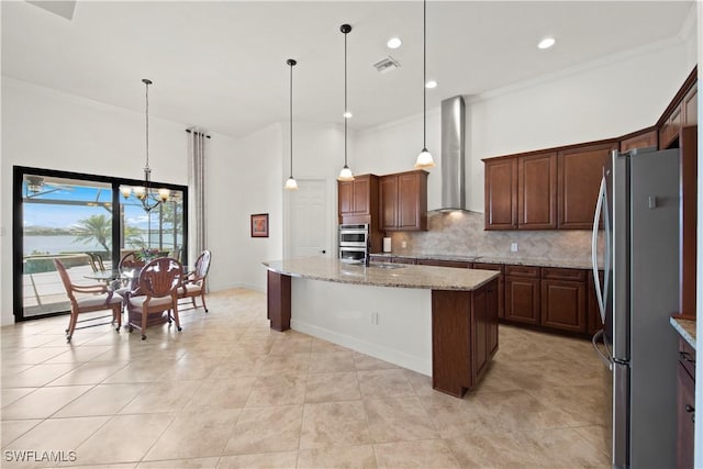 kitchen featuring appliances with stainless steel finishes, pendant lighting, a center island with sink, and wall chimney range hood