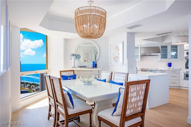 dining space with a chandelier, a raised ceiling, and light hardwood / wood-style flooring