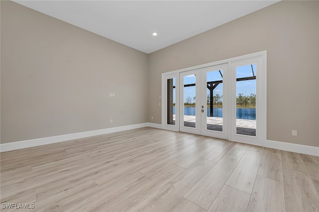 empty room with french doors, a water view, and light hardwood / wood-style floors