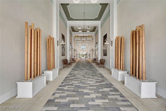 hallway with a tray ceiling, a notable chandelier, and a high ceiling