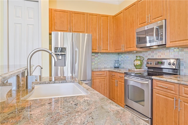 kitchen featuring tasteful backsplash, light stone countertops, stainless steel appliances, and sink