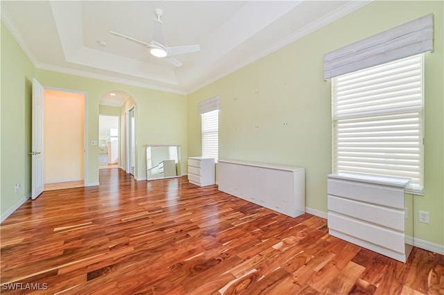 empty room with ornamental molding, a tray ceiling, wood-type flooring, and ceiling fan