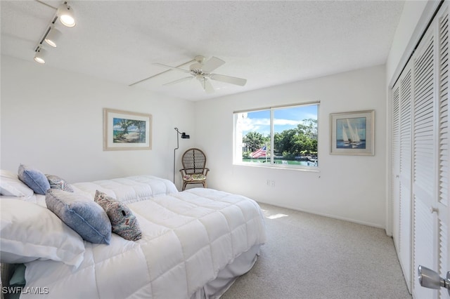 bedroom with track lighting, ceiling fan, a textured ceiling, a closet, and light colored carpet