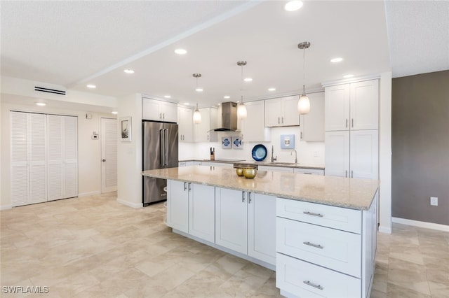 kitchen featuring white cabinets, stainless steel appliances, pendant lighting, wall chimney exhaust hood, and a center island