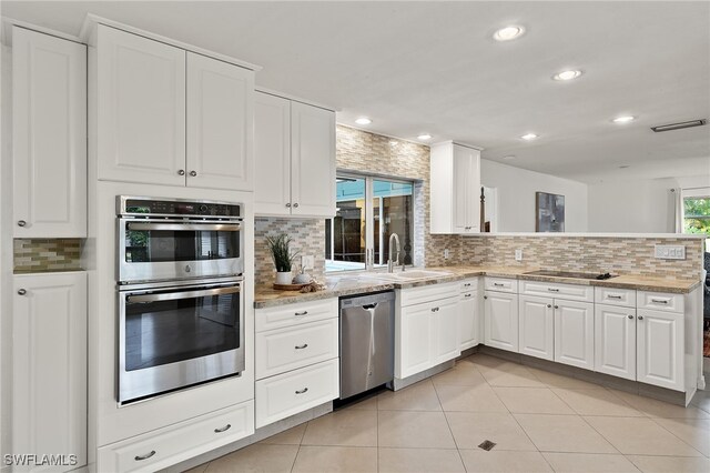 kitchen with light stone counters, stainless steel appliances, white cabinetry, and light tile patterned flooring