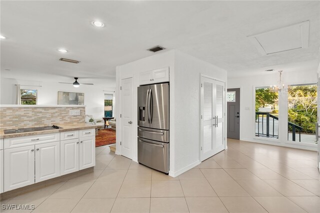 kitchen with stainless steel fridge, backsplash, ceiling fan with notable chandelier, white cabinets, and light tile patterned flooring