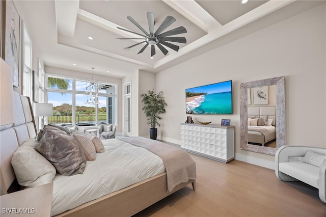 bedroom with ceiling fan with notable chandelier, light wood-type flooring, and a raised ceiling