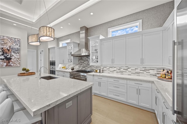 kitchen featuring a large island with sink, white cabinetry, wall chimney exhaust hood, sink, and premium appliances