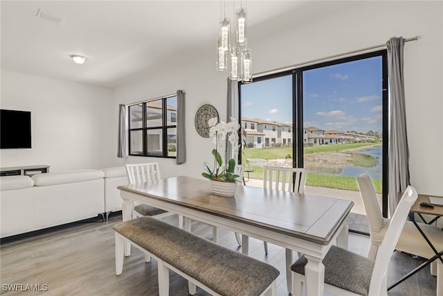 dining room featuring a notable chandelier, a water view, and light wood-type flooring