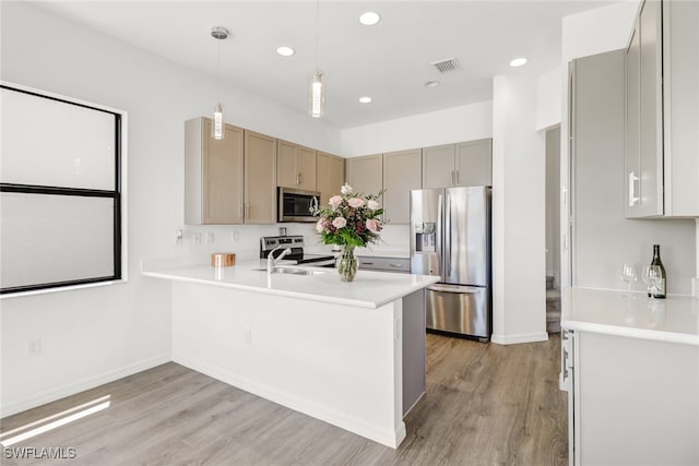 kitchen with pendant lighting, kitchen peninsula, appliances with stainless steel finishes, and light hardwood / wood-style flooring