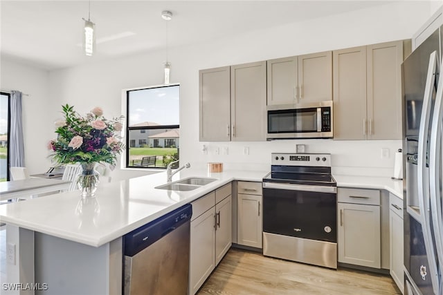 kitchen featuring sink, hanging light fixtures, kitchen peninsula, light hardwood / wood-style floors, and appliances with stainless steel finishes