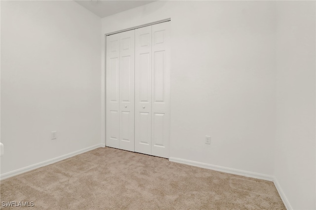 unfurnished bedroom with light colored carpet and a closet