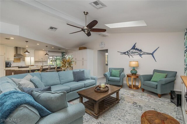 living room featuring ceiling fan and vaulted ceiling with skylight