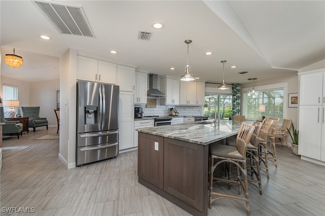 kitchen featuring white cabinets, appliances with stainless steel finishes, wall chimney exhaust hood, and a spacious island