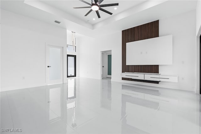 unfurnished living room with ceiling fan, light tile patterned flooring, and a raised ceiling