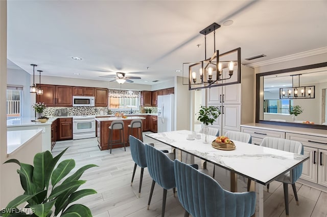 dining space with ceiling fan with notable chandelier, light hardwood / wood-style floors, and ornamental molding