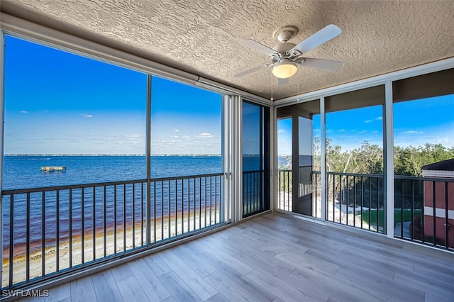 unfurnished sunroom with ceiling fan and a water view