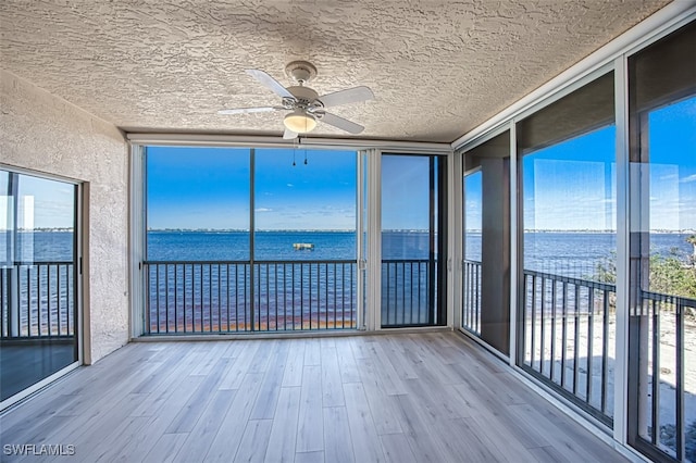 unfurnished sunroom featuring ceiling fan and a water view