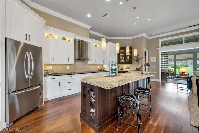 kitchen with a kitchen island with sink, dark hardwood / wood-style floors, wall chimney exhaust hood, pendant lighting, and appliances with stainless steel finishes