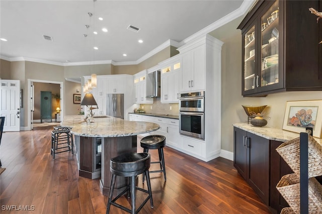 kitchen featuring a large island with sink, dark hardwood / wood-style floors, stainless steel appliances, crown molding, and pendant lighting