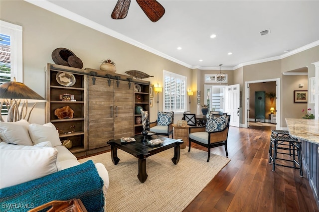 living room with crown molding, a barn door, dark wood-type flooring, and ceiling fan