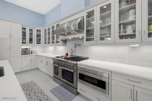 kitchen with built in microwave, wall chimney exhaust hood, tasteful backsplash, range with two ovens, and white cabinets