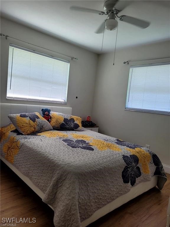 bedroom with ceiling fan, multiple windows, and dark hardwood / wood-style flooring