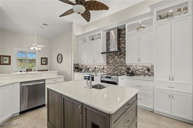 kitchen featuring white cabinets, an island with sink, wall chimney range hood, and appliances with stainless steel finishes