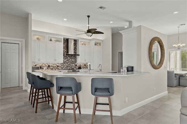 kitchen featuring white cabinetry, wall chimney range hood, hanging light fixtures, and a breakfast bar area