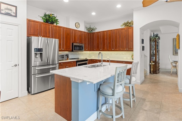 kitchen featuring backsplash, a center island with sink, sink, appliances with stainless steel finishes, and a breakfast bar area