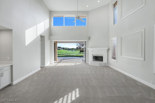 unfurnished living room with light carpet, ceiling fan, and a high ceiling