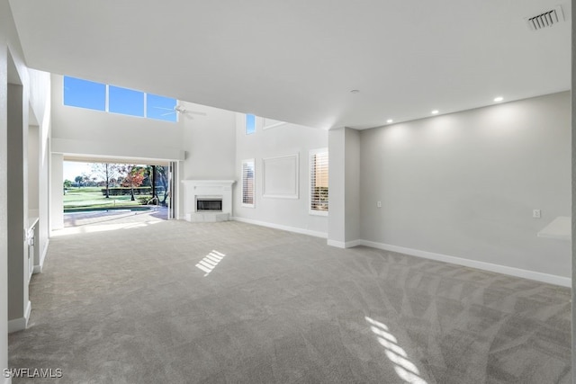 unfurnished living room featuring a towering ceiling, carpet floors, and ceiling fan