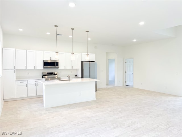 kitchen with a center island with sink, appliances with stainless steel finishes, pendant lighting, white cabinets, and light hardwood / wood-style flooring