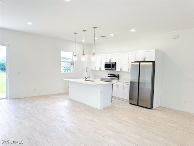 kitchen featuring appliances with stainless steel finishes, pendant lighting, sink, white cabinets, and a kitchen island with sink